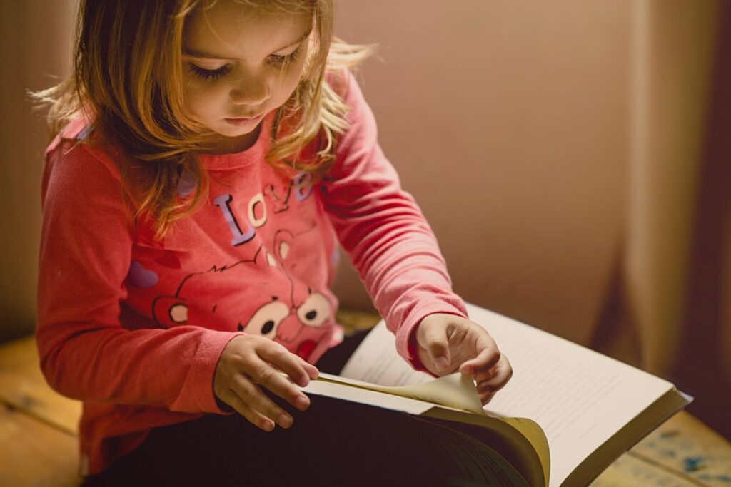 A young girl wearing a pink shirt reads a book.