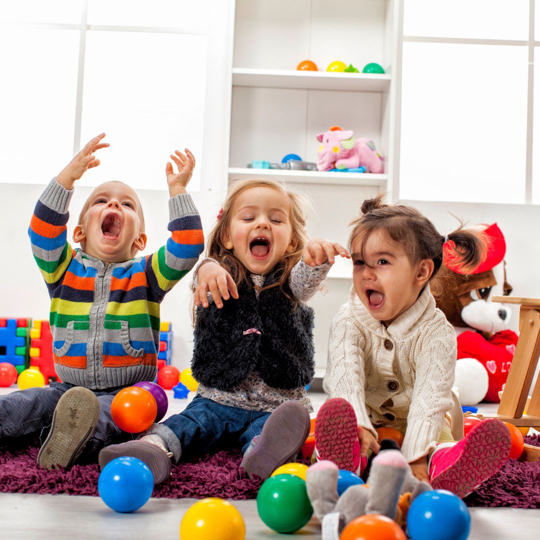 Three young kids laughing and tossing around colorful balls
