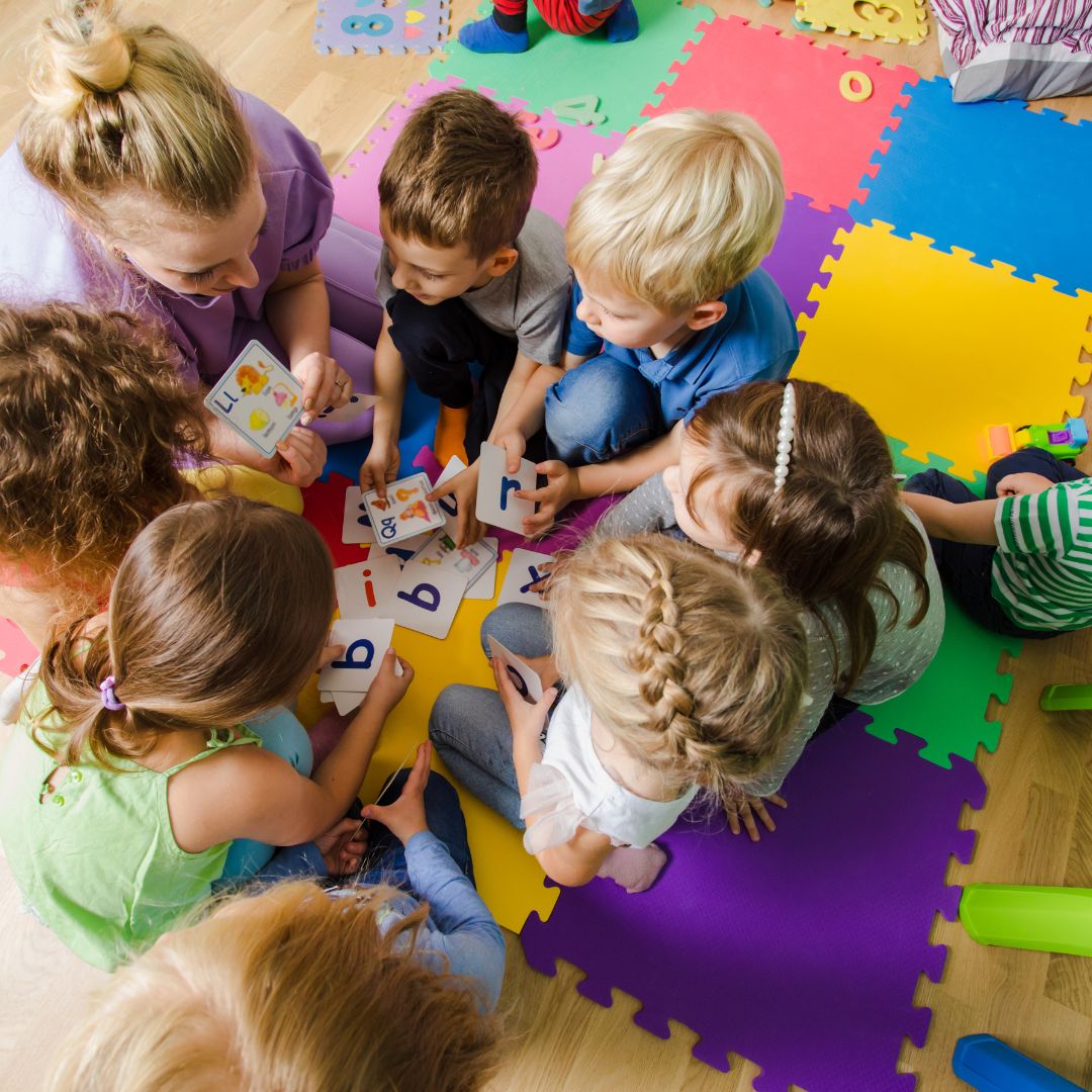 A group of seven children and one teacher on foam mats playing with letter cards
