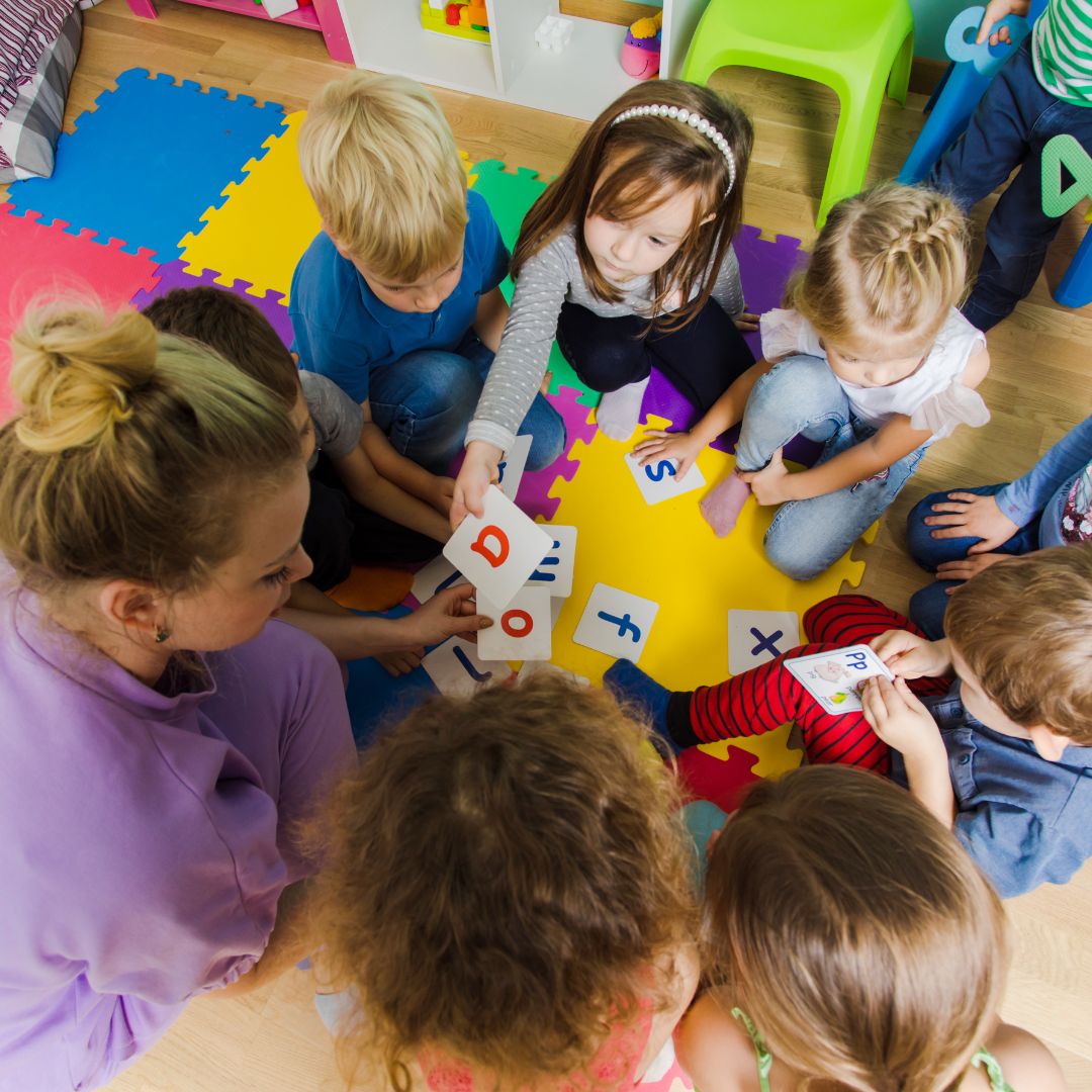 Daycare children, sitting in a circle, working with letter flashcards with a daycare teacher