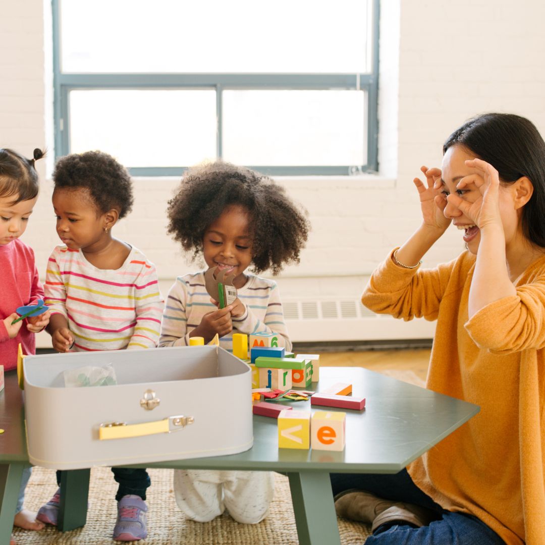 Daycare teacher making a silly face at toddlers playing with blocks
