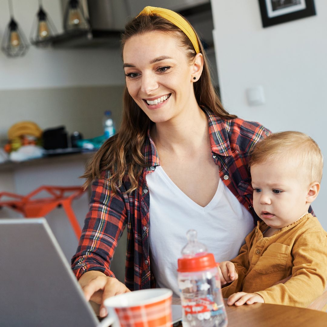 a woman holding a toddler while doing research on a computer