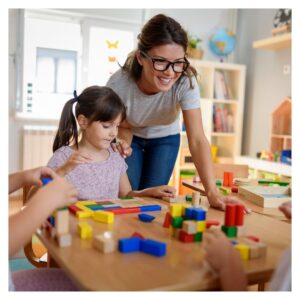 teacher leans over a table where a girl sits with colored blocks 