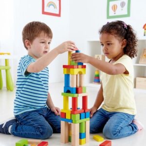 Two focused young children carefully stack colorful wooden blocks on a clean classroom floor.