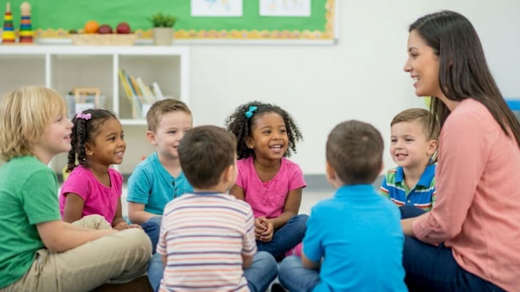 Preschoolers smiling and laughing during story time with their teacher in a bright classroom.